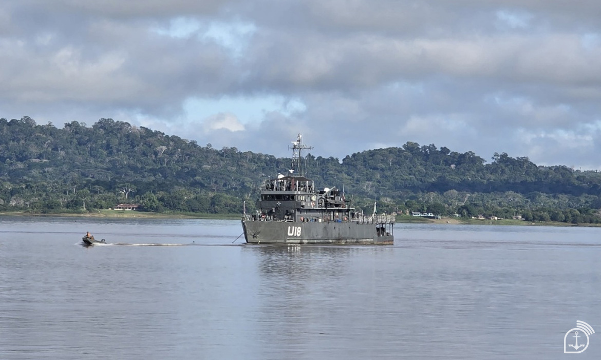 Navio militar em rio cercado por floresta.