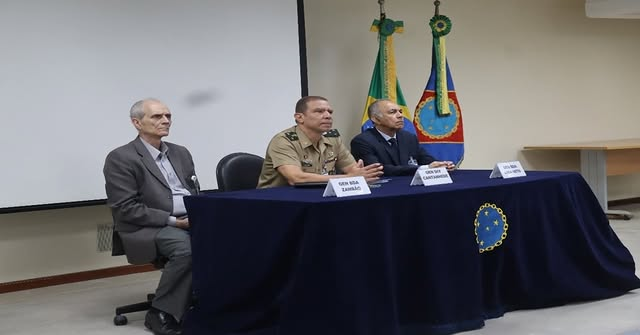 Três homens em conferência com bandeiras ao fundo.