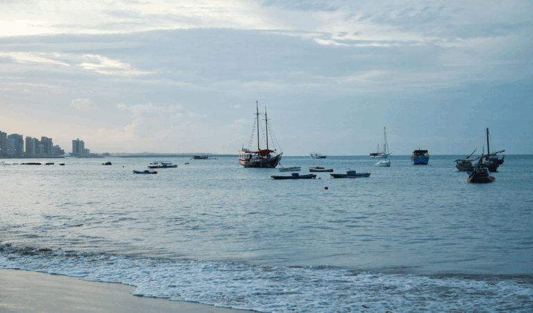 Barcos no mar ao entardecer, prédios ao fundo.