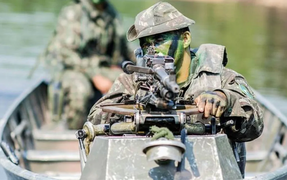 Soldado em barco com arma na floresta.