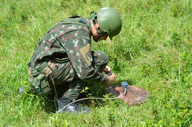 Soldado desarmando mina terrestre em campo gramado.