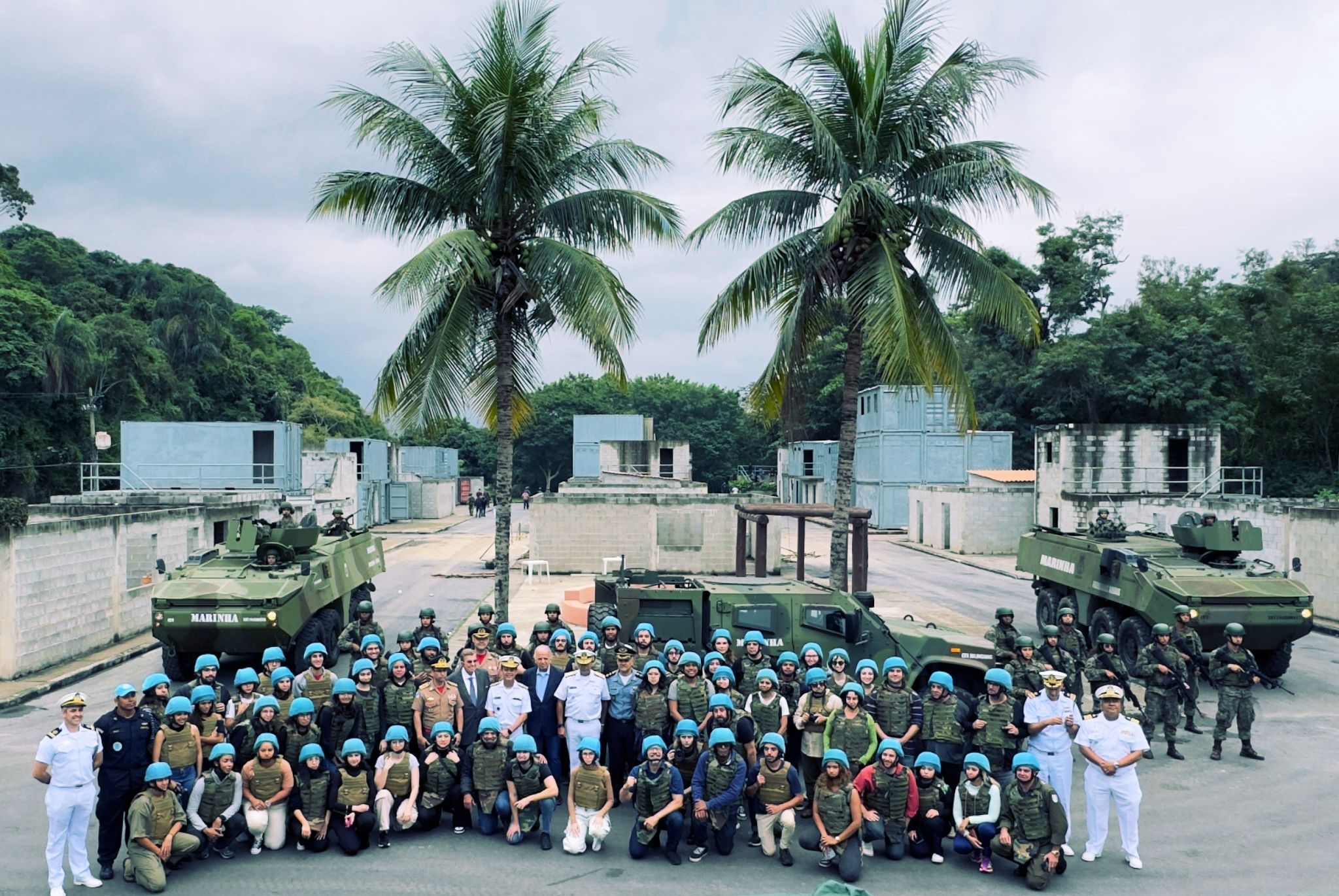 Grupo militar e civil em base com tanques.