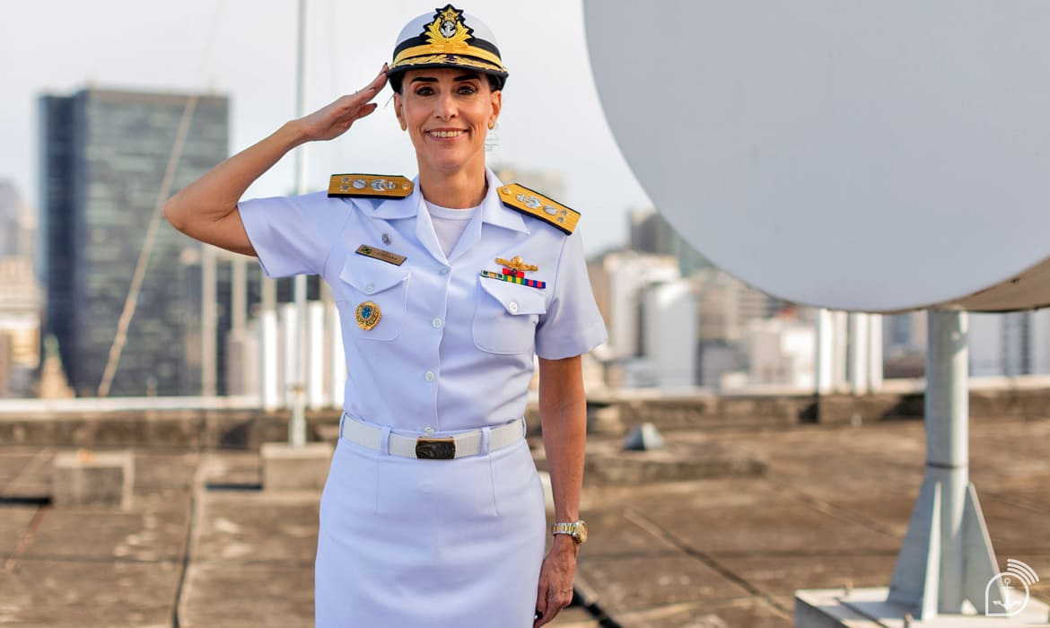Mulher militar saudando em uniforme branco ao ar livre.