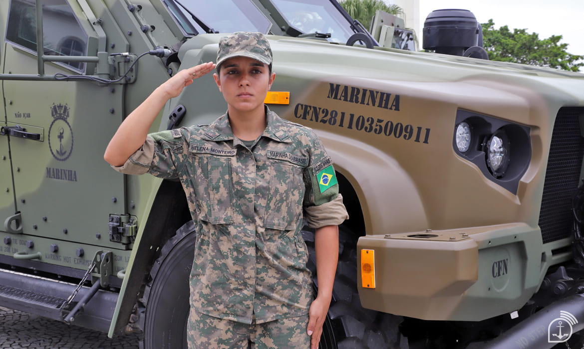 Militar fardada saúda em frente a veículo militar.