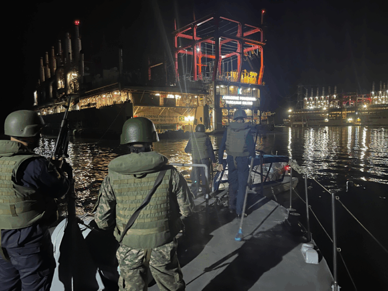 Soldados em barco patrulhando perto de usinas à noite.