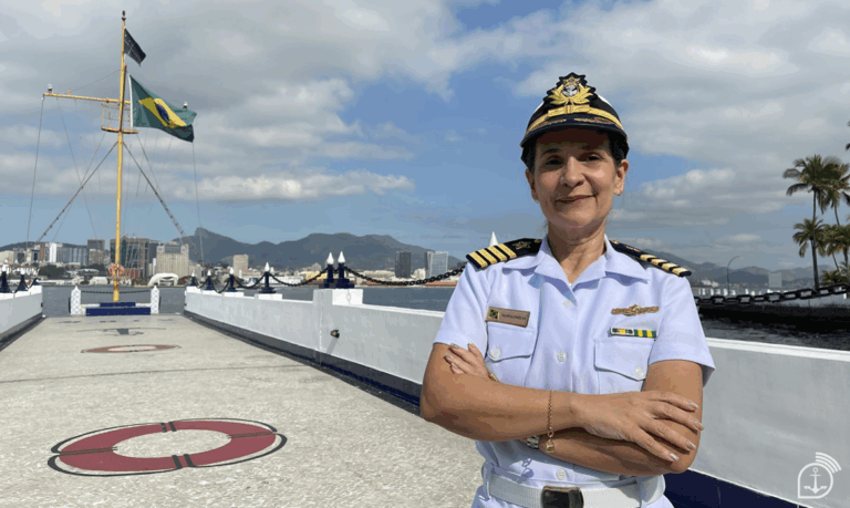 Oficial naval em uniforme, bandeira do Brasil ao fundo.