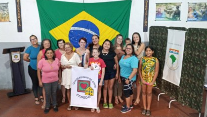 Grupo em evento com bandeira do Brasil ao fundo.