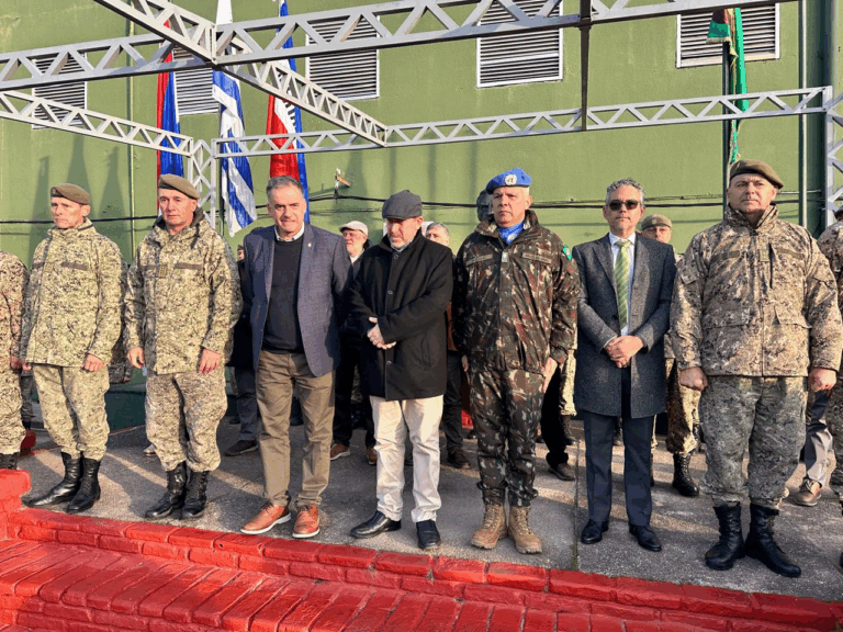 Grupo militar em evento com bandeiras ao fundo.