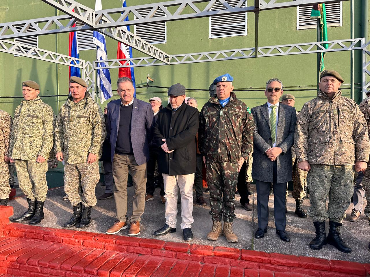 Grupo militar em evento com bandeiras ao fundo.