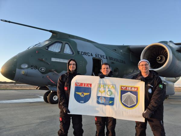 Pessoas seguram banner em frente a avião militar.
