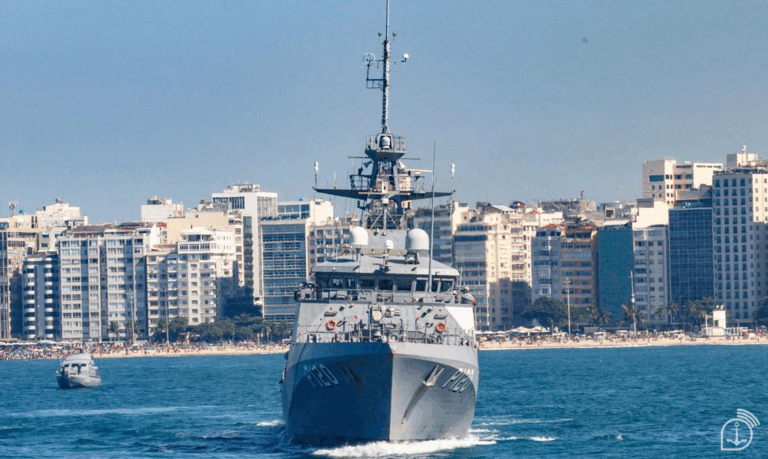 Fragata navegando em frente a prédios na cidade costeira.
