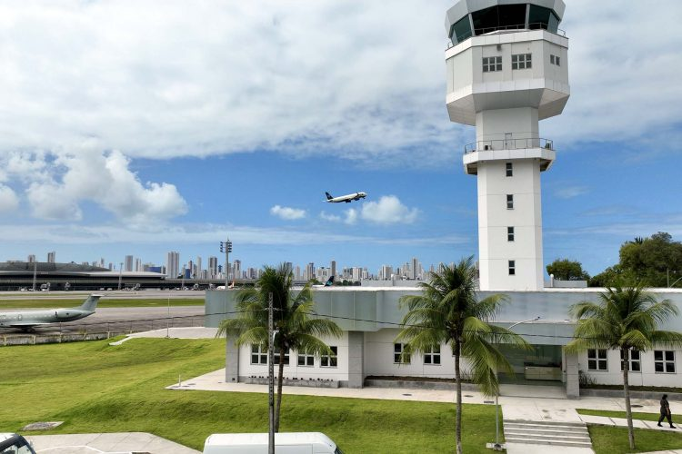 Aeroporto com torre e avião no céu.
