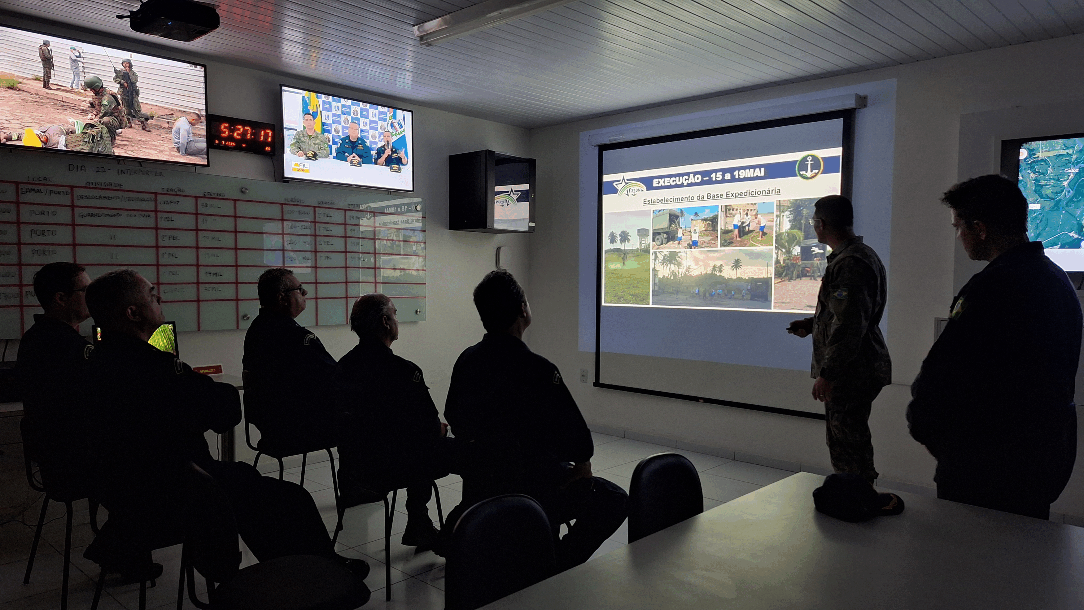 Militares assistem apresentação em sala de controle.