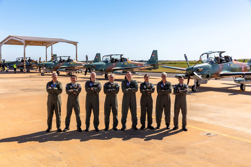 Pilotos da força aérea com aviões militares ao fundo.